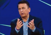 A focused Sunil Gavaskar sits in a cricket studio wearing a navy blazer and striped shirt, gesturing as he speaks about Indian cricket board reforms against a blue‑green background.